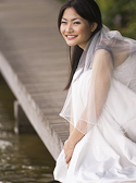 A beautiful asian bride sits on a boardwalk at the edge of a lake